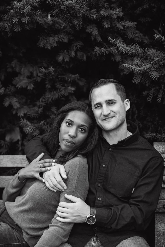 Black and white photo of a woman leaning on her partner on a park bench enjoying their Central Park engagement photoshoot